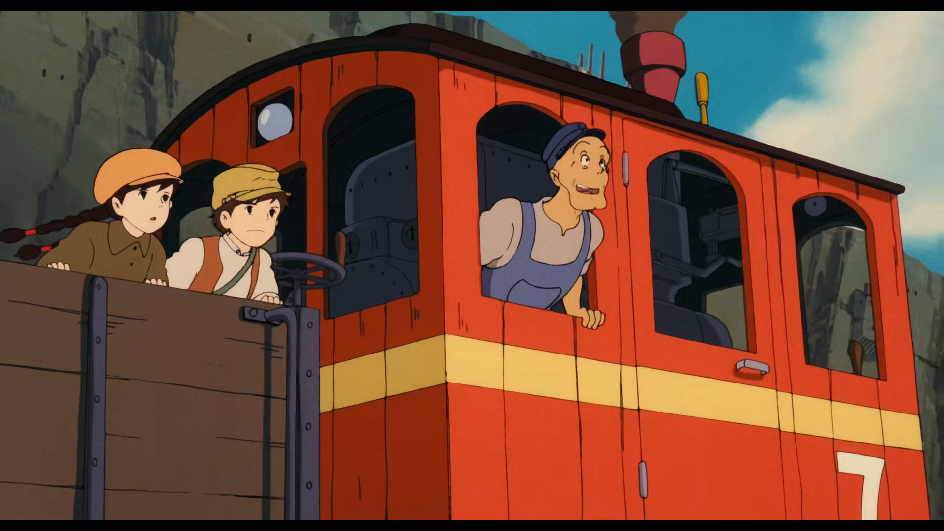 Scène du Chateau dans le Ciel
Une locomotive rouge avec une bande jaune sous les fenêtres, une cheminée couleur bordeaux et dont on distingue la grosse chaudière noire, tirant un wagon ouvert en bois.
Dans le wagon se trouvent Sheeta, jeune fille aux cheveux noirs coiffés en deux longues nattes, yeux noirs, portant une chemise kaki et un béret orange, ainsi que Pazu, jeune garçon aux cheveux noirs et aux yeux noirs, portant un haut clair avec un gilet marron, une casquette jaune moutarde, ainsi qu'un sac en bandoulière, tandis que dans la locomotive, se tient le conducteur, un adulte chauve à la mâchoire carrée, avec un haut gris, une salopette et une casquette bleues. Iels fixent toustes quelque chose hors champ qui est en hauteur avec appréhension.
L'environnement est rocheux avec des falaises droites qui tombent à pic, indiquant qu'on est dans une carrière de pierres. 