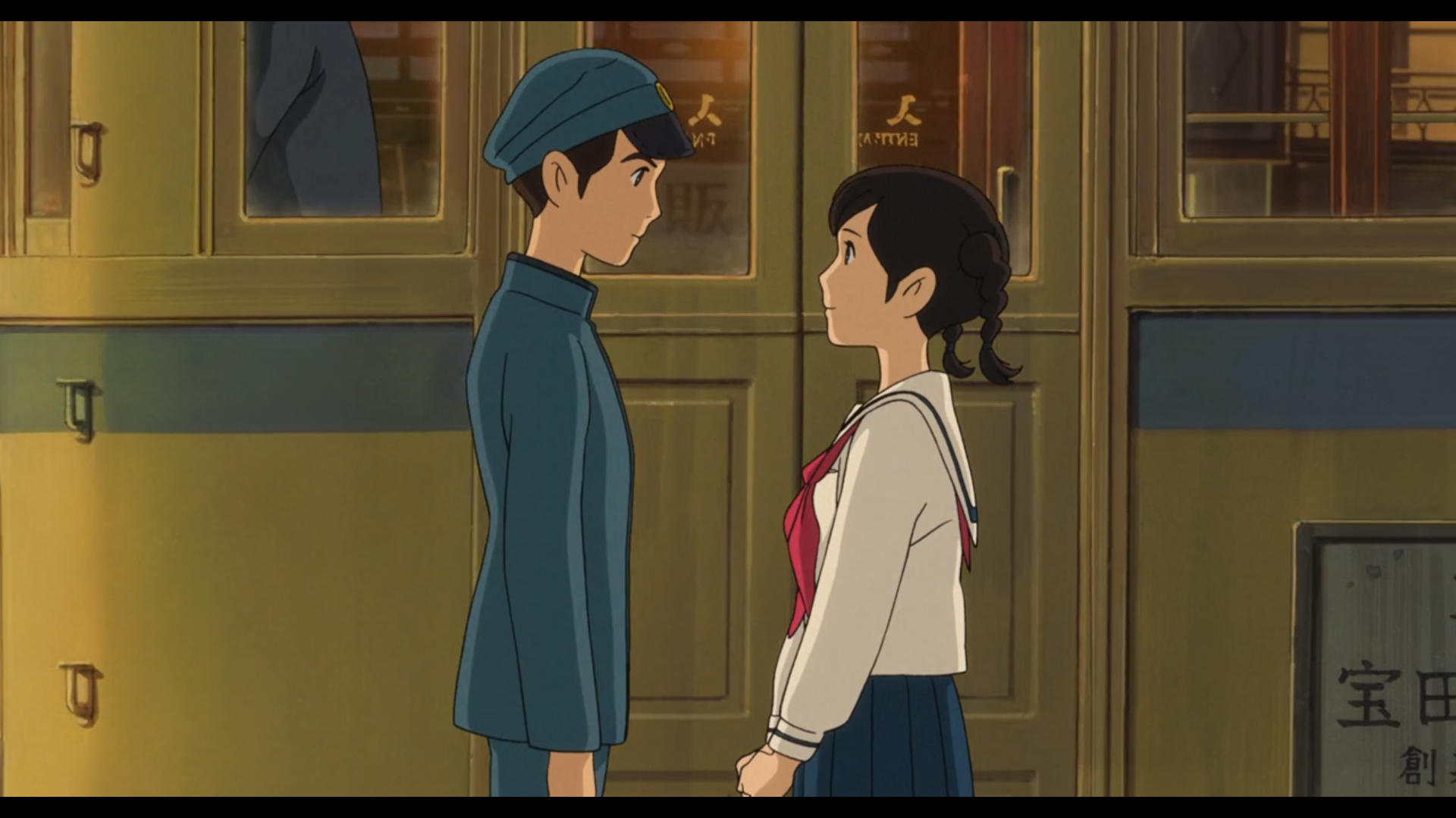 Scène de la Colline aux coquelicots
A droite, Shun, adolescent japonais, cheveux noirs, yeux noirs, portant un uniforme de lycéen et une casquette bleus, de profil fait face à Umi, adolescente japonaise, cheveux noirs coiffés en couettes, yeux noirs, portant une chemise blanche, une jupe bleue et un ruban rose autour du cou.
Chacun semble avoir une expression tendre pour l'autre.
Derrière, se trouve une rame de tram jaune, avec une bande bleue sous les fenêtres, et on peut distinguer à travers une fenêtre, les habits bleus du conducteur
Une pénombre enveloppe la scène, indiquant qu'il fait nuit.