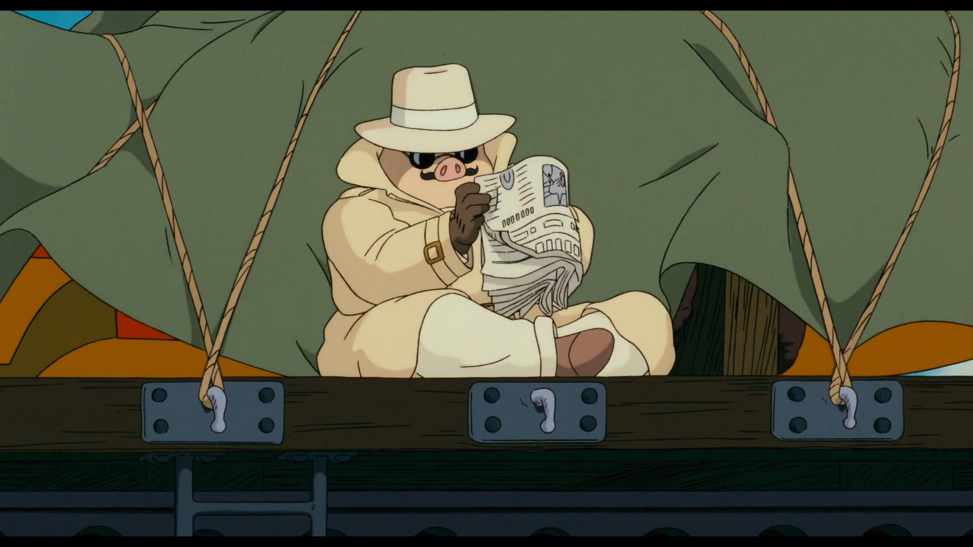Scène de Porco Rosso
Porco Rosso, cochon anthropomorphique, habillé d'une veste beige, d'un pantalon et d'un chapeau clairs, de chaussures marrons et de gants sombres, portant des lunettes noires et des moustaches frisées sous son groin, assis en tailleur à l'arrière d'un wagon ouvert, tenant un journal entre ses mains.
Derrière lui, une bâche vert kaki, cachant un objet orange (son avion), tenue par des cordes fixées à la limite du wagon.